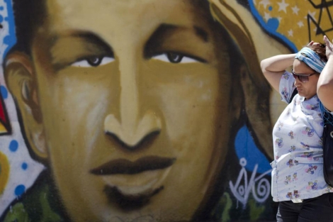 Una mujer pasea en Caracas frente a un mural de Chávez.| Reuters