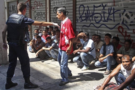 Un policía griego mantiene retenidos a unos inmigrantes residentes en Atenas.| Efe/Pantelis Saitas